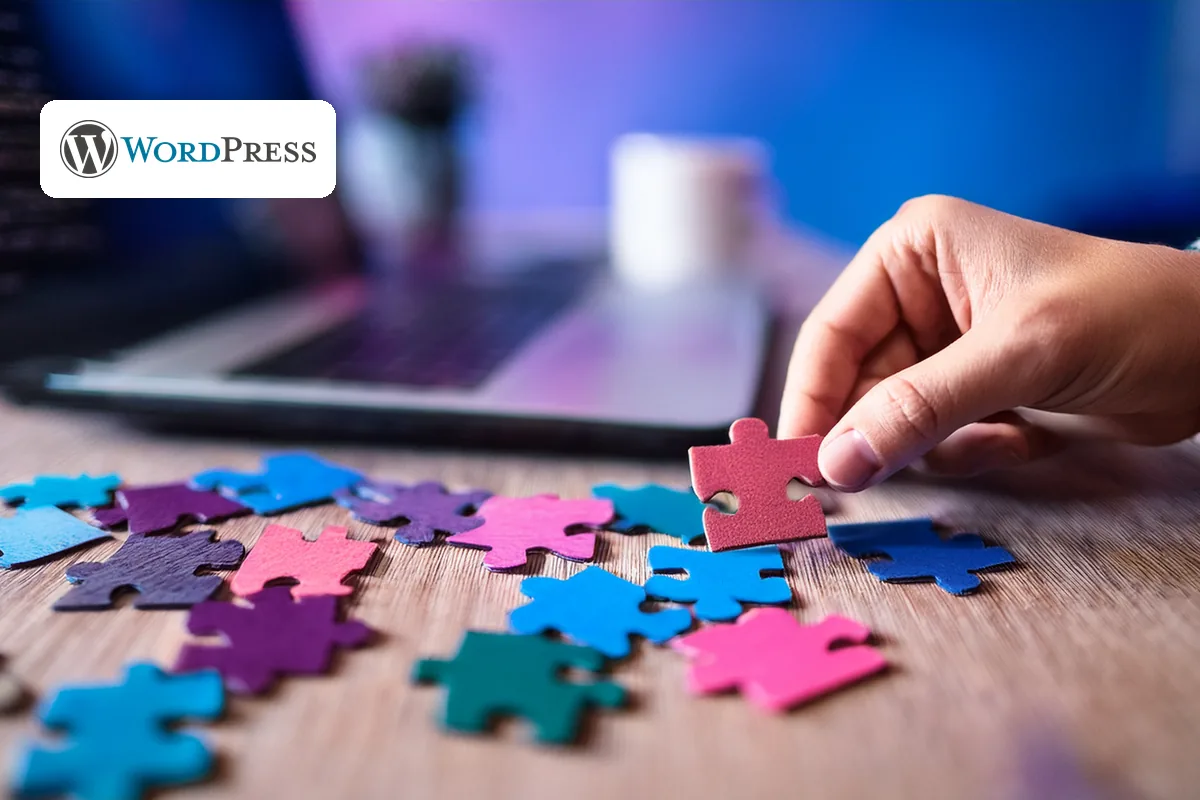 Accessible WordPress plugins: hand placing colourful puzzle pieces beside a laptop, WordPress logo