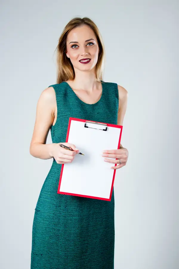 A woman in a green dress holding out a red clipboard with a blank sheet and a pen.