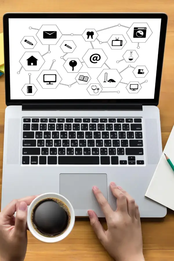 A laptop on a wooden desk showing a network of connected icons, a coffee cup beside it.