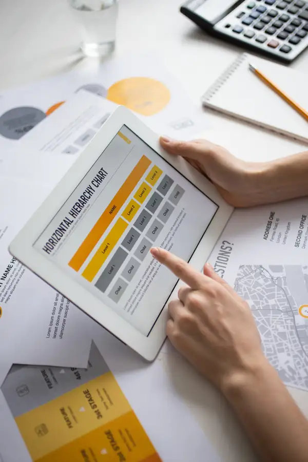 A tablet showing a hierarchy chart on a desk with a calculator, pencil and printed charts.