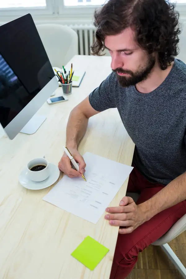 A man at a desk filling in a printed form beside a cup of coffee.