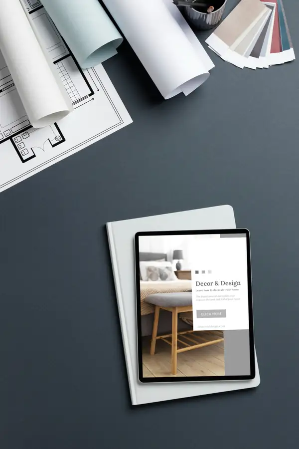 A tablet on a notebook beside rolled floor plans and a fan of colour swatches.