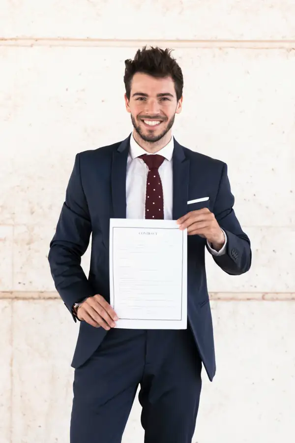 A consultant in a suit holding out a signed contract document towards the viewer.