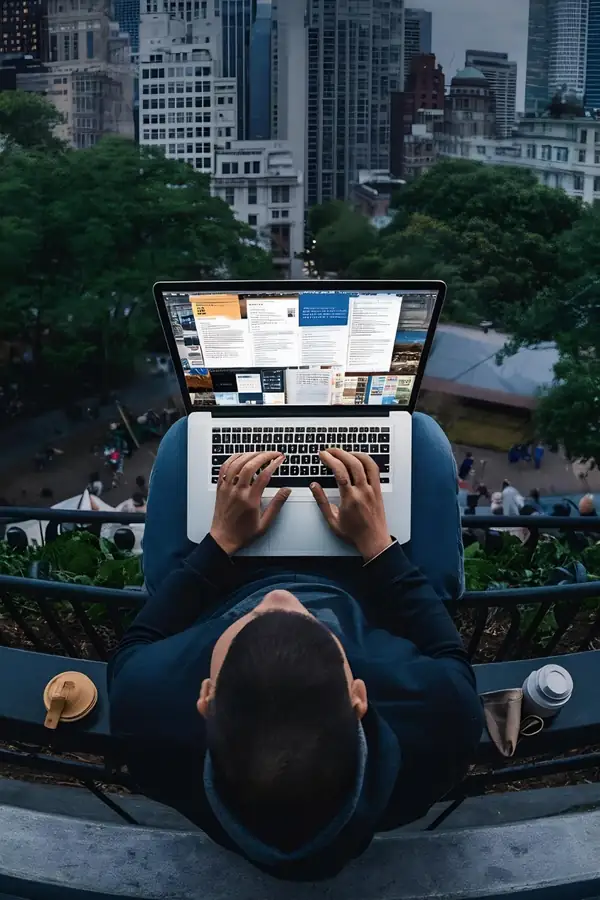 Seen from above, a person working alone on a laptop on a bench with a city behind them.