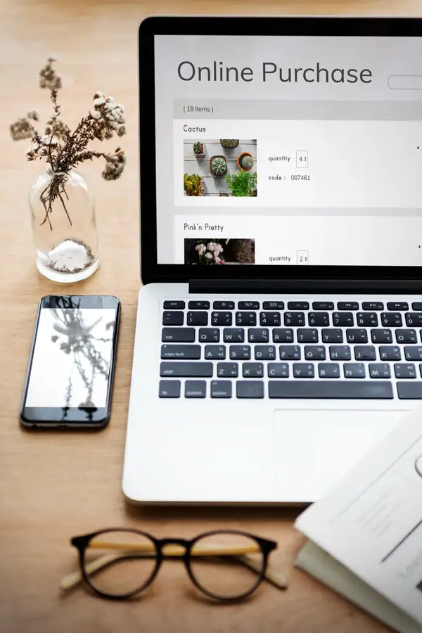 A laptop on a desk showing an online shopping cart with product rows and quantity fields.