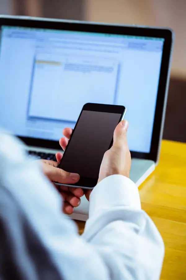 A man holding a phone in front of a laptop showing an open document.