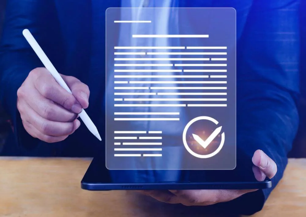 A person in a blue suit holds a tablet showing a checked document, with a stylus in the other hand.