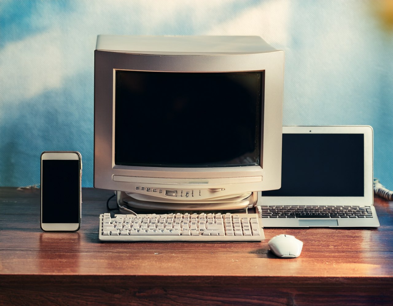 Old CRT computer next to a modern laptop and smartphone