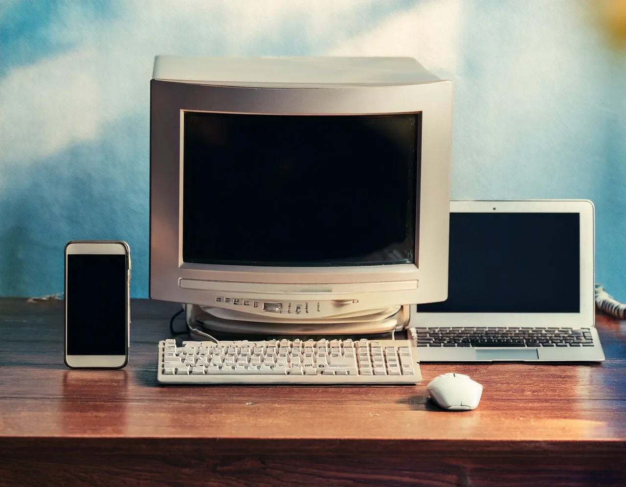 Old CRT computer next to a modern laptop and smartphone