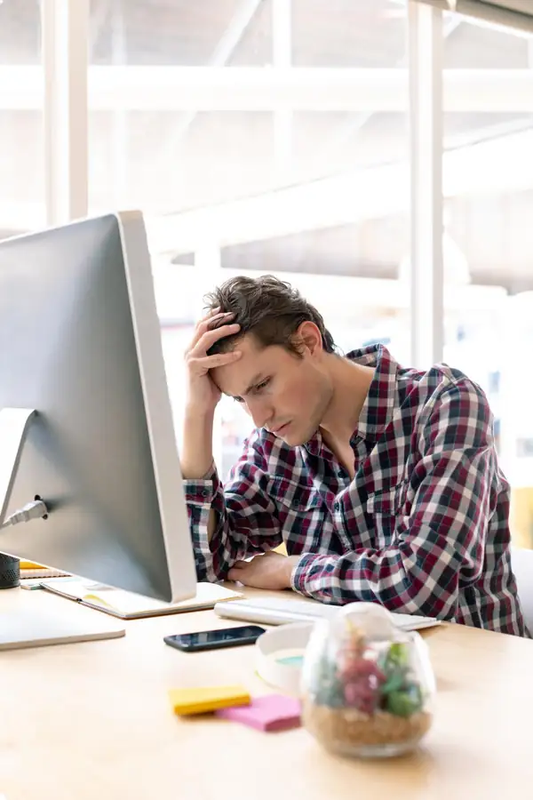 A man at a desktop computer resting his head on his hand, frustrated by what is on screen.